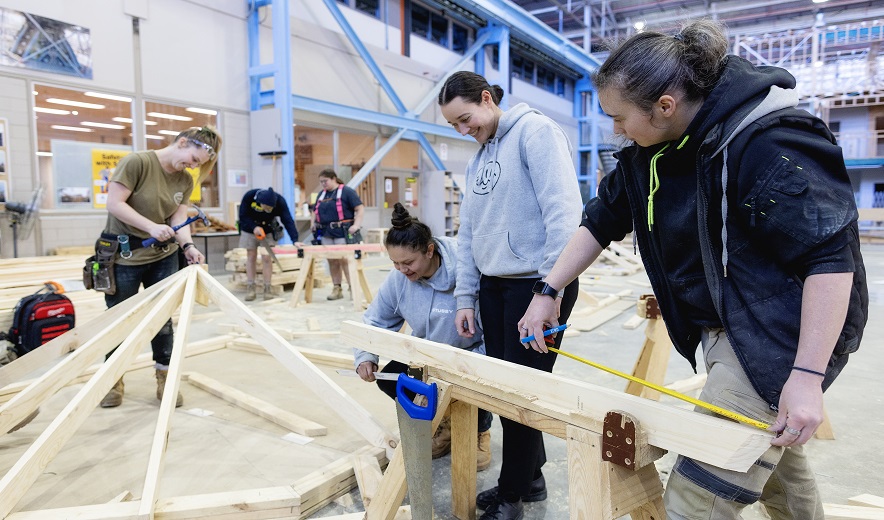 Four female apprentices work on a carpentry frame together in a trades' training workshop.