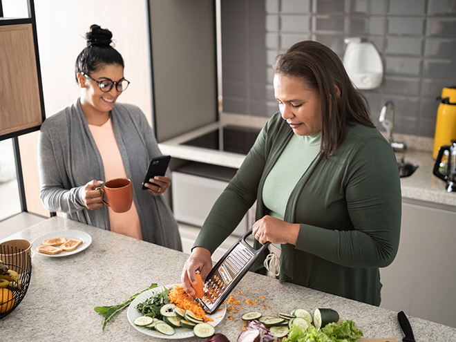 Lesbian couple using smartphone and preparing vegetables at home