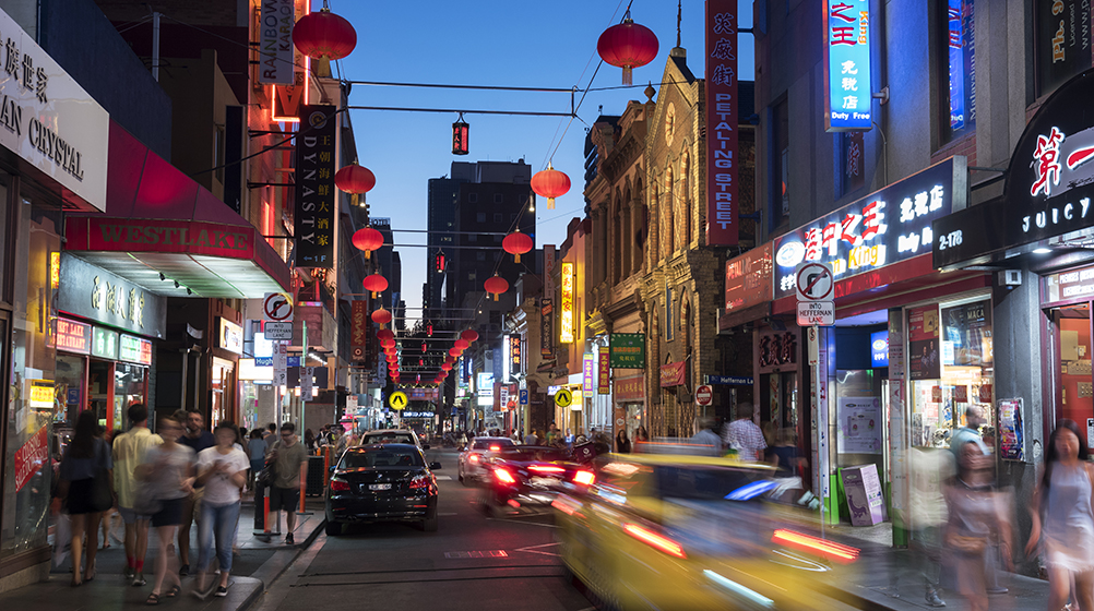 Taxi drives through Melbourne's busy Chinatown, Little Bourke Street, at dusk.